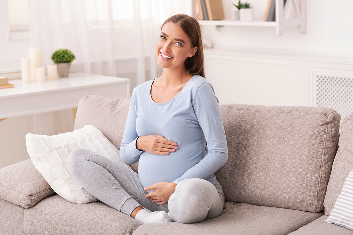 pregnant touching belly smiling sitting on couch pregnant touching belly smiling sitting on couch