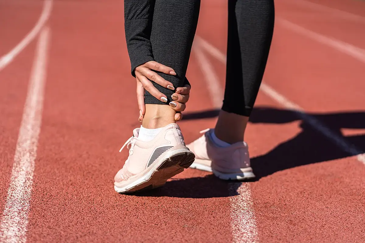close up of athletic woman runner touching foot in pain due to sprained ankle rear view