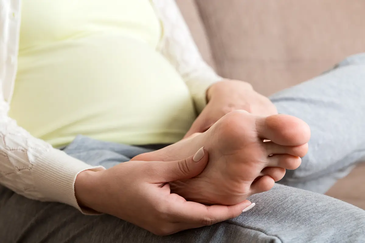 closeup of hands massaging swollen foot while sitting on sofa closeup of hands massaging swollen foot while sitting on sofa
