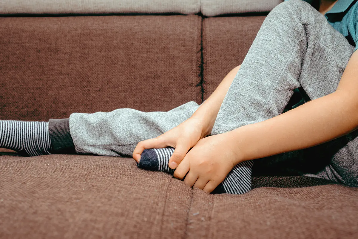 the little boy is holding his foot he feels strong foot pain the little boy is holding his foot he feels strong foot pain