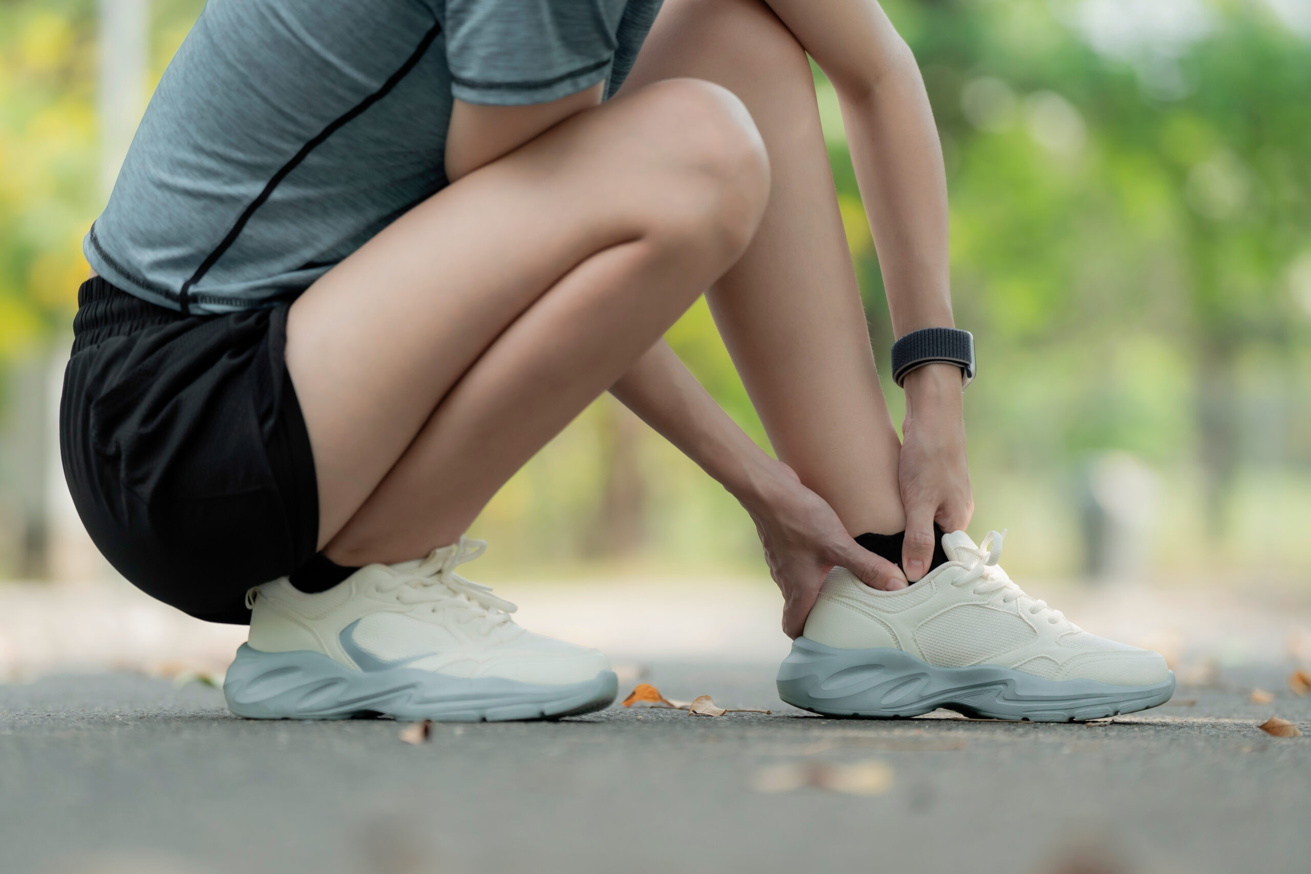Young woman suffering ankle pain after running in park, squatting and holding injured foot, sports injury and sprained ankle outdoor fitness concept. workout, foot, sprain, strain, ankle, pain, injury Common Foot & Ankle Injuries in Youth & High School Athletes